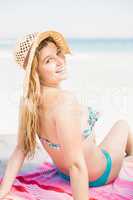 Pretty woman in bikini and beach hat sitting on the beach