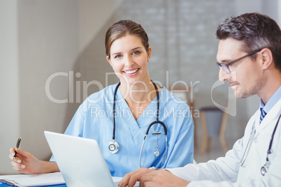 Portrait of smiling doctor sitting at desk with colleague