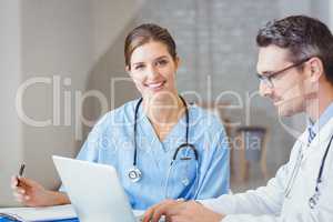 Portrait of smiling doctor sitting at desk with colleague