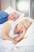 Smiling senior woman sleeping besides husband on bed