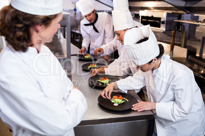 Head chef overlooking other chef decorating dish
