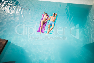 Couple relaxing on inflatable raft at swimming pool