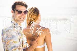 Man making a sun symbol on womans back while applying a sunscree
