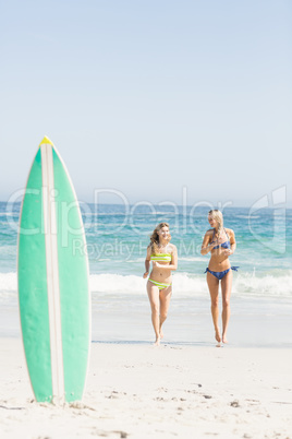 Surfboard in sand and two women running on the beach