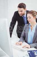 Businessman looking in computer monitor while colleague typing