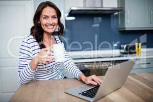 Portrait of smiling young woman working on laptop while holding