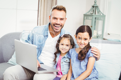 Father and daughters with laptop sitting on sofa
