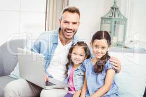 Father and daughters with laptop sitting on sofa