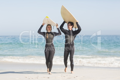 Happy couple in wetsuit carrying surfboard over the head