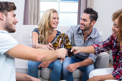 Cheerful friends toasting beer while sitting on sofa