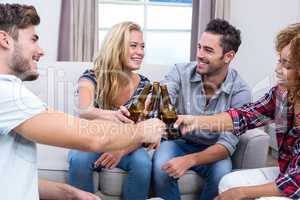 Cheerful friends toasting beer while sitting on sofa