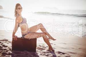 Glamorous woman in bikini sitting on an old suitcase