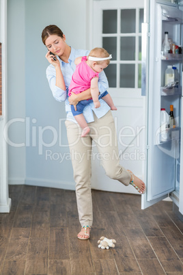 Woman closing refrigerator door while carrying baby girl
