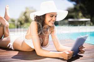 Happy woman in hat using digital tablet by pool side