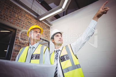 Architect pointing with colleague holding blueprint