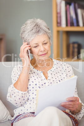 Senior woman holding mobile phone while looking documents