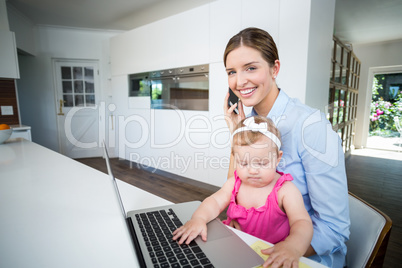 Woman using mobile phone with baby girl by laptop