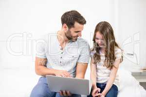 Father showing laptop to daughter on bed