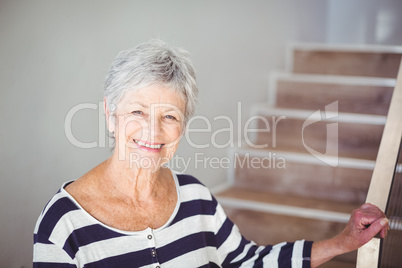 Portrait of happy senior woman against staircase