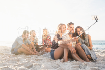 Smiling friends sitting on sand singing and taking selfies