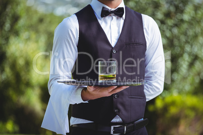 Handsome waiter holding a tray with glass of whiskey