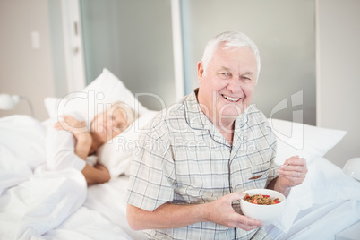 Happy senior man having salad by sleeping wife