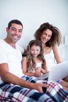 Portrait of couple using laptop with their daughter on bed