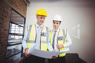Architects discussing while holding blueprint