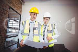Architects discussing while holding blueprint