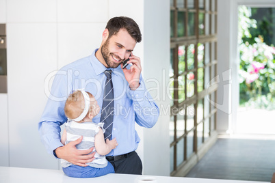 Businessman talking on cellphone while holding daughter Businessman talking on cellphone while holding daughter
