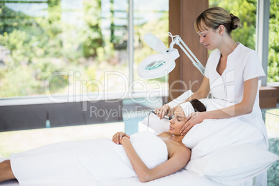 Young woman relaxing on bed while receiving facial massage