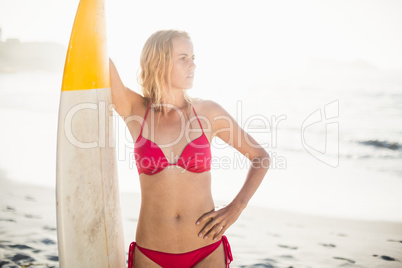 Woman in bikini standing with a surfboard on the beach