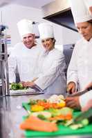 Two chefs smiling at camera while chopping vegetables