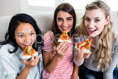 Beautiful female friends eating pizza at home