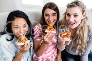 Beautiful female friends eating pizza at home