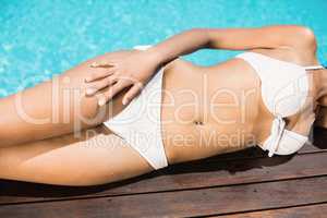 Mid section of a woman in white bikini lying by pool side