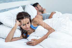 Woman using phone while relaxing on bed husband in background
