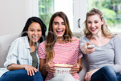 Cheerful female friends with remote and popcorn at home