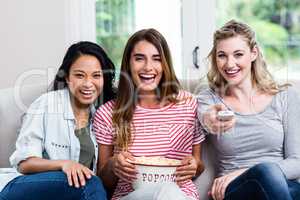 Cheerful female friends with remote and popcorn at home