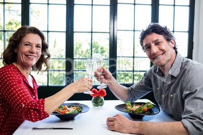 Middle-aged couple toasting champagne flutes while having lunch