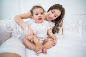 Mother playing with baby girl on bed