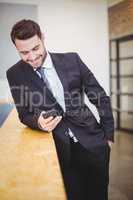 Businessman looking in cellphone while leaning on counter