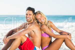 Happy couple sitting back to back on beach