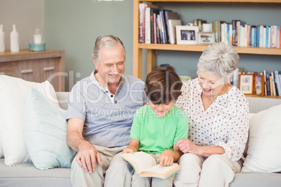 Grandparents assisting grandson while reading book in sitting ro