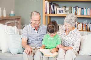 Grandparents assisting grandson while reading book in sitting ro