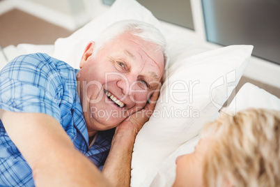 Portrait of happy man lying with wife on bed