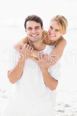 Man giving a piggy back to woman on the beach