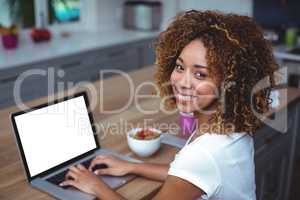 Young woman smiling while using laptop in kitchen