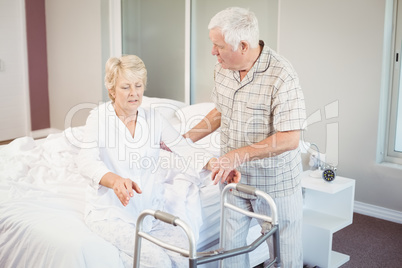 Senior man assisting ill woman in getting up from bed