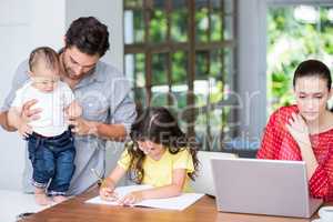 Mother using laptop daughter doing homework with father